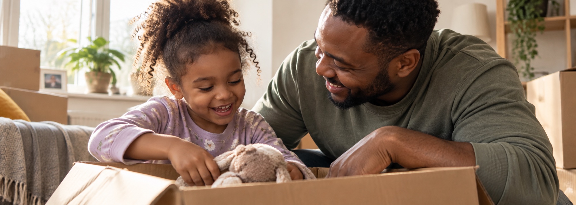 A father and his young daughter unpacking a box of toys in a new home
