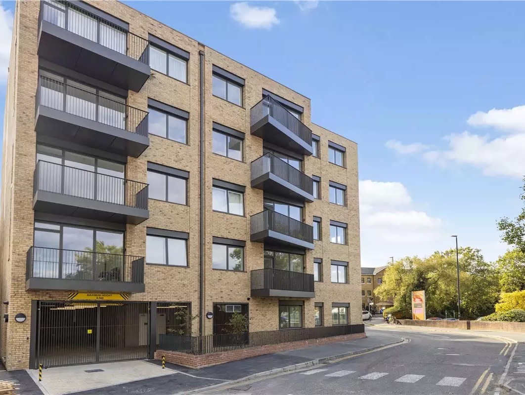 A newly built block of flats in pale brick with balconies on a London street